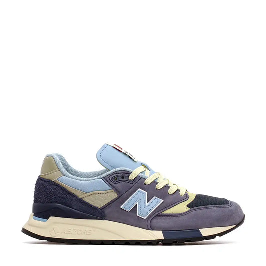 Athletic sneaker in navy, light blue, and pale yellow color scheme with New Balance branding.