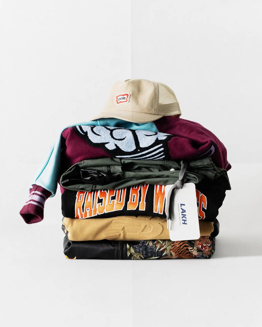 Neatly folded stack of casual clothing topped with a beige baseball cap.