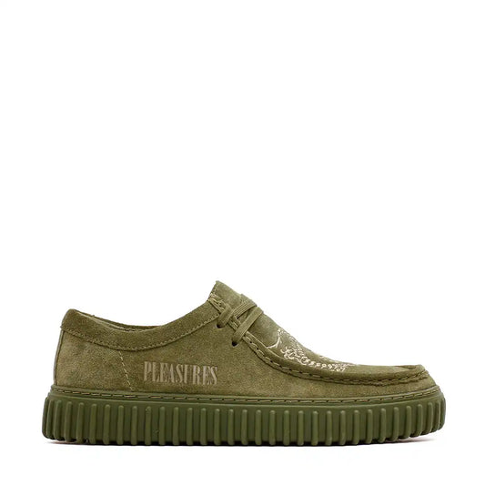 Olive green suede wallabee-style sneaker with ribbed platform sole and ’PLEASURES’ branding.